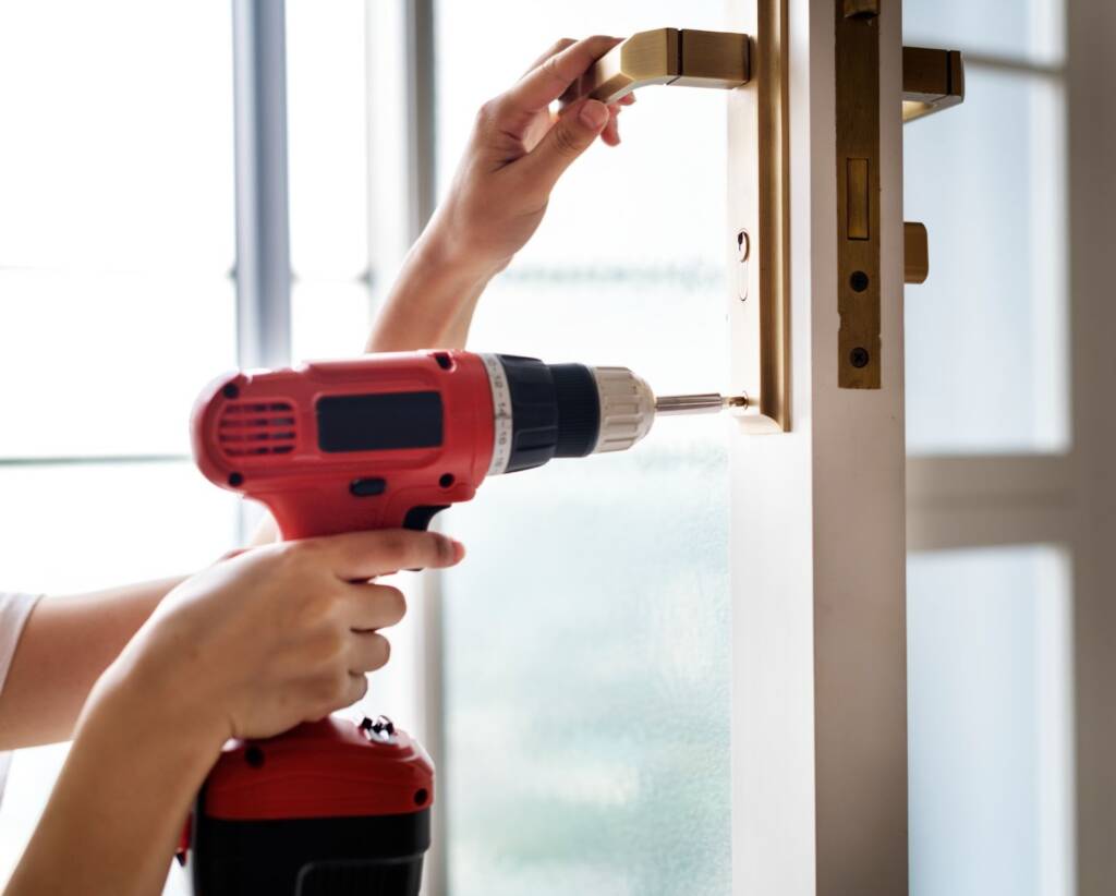 Woman locksmith drilling to fit a new lock on a commercial door
