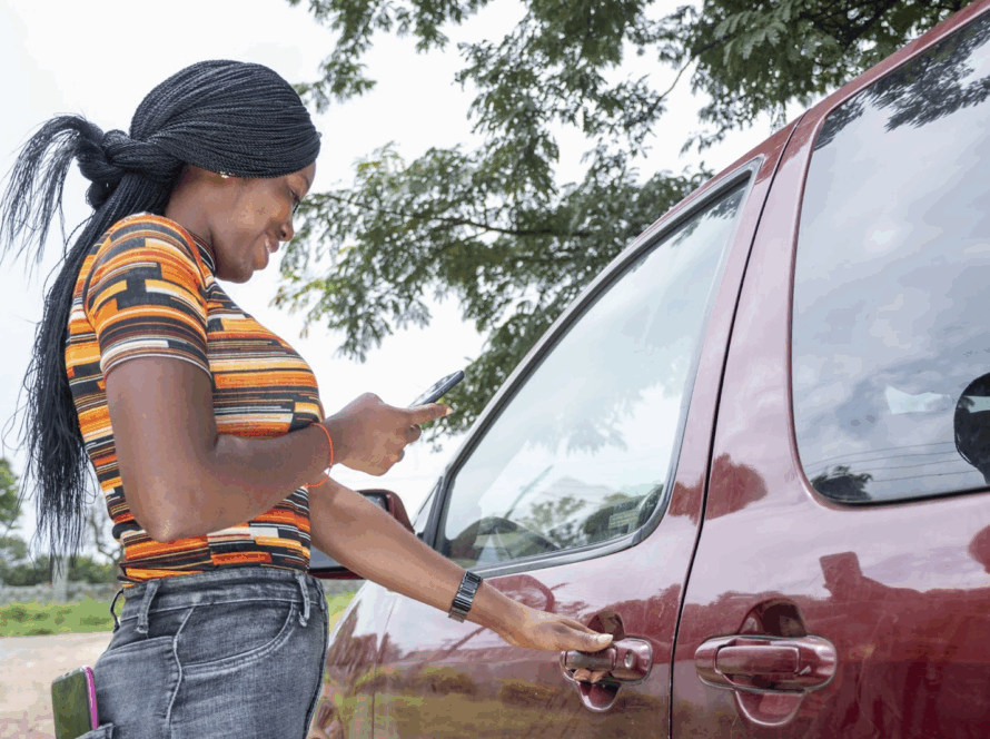 A woman is using her phone while trying to unlock her gray car.