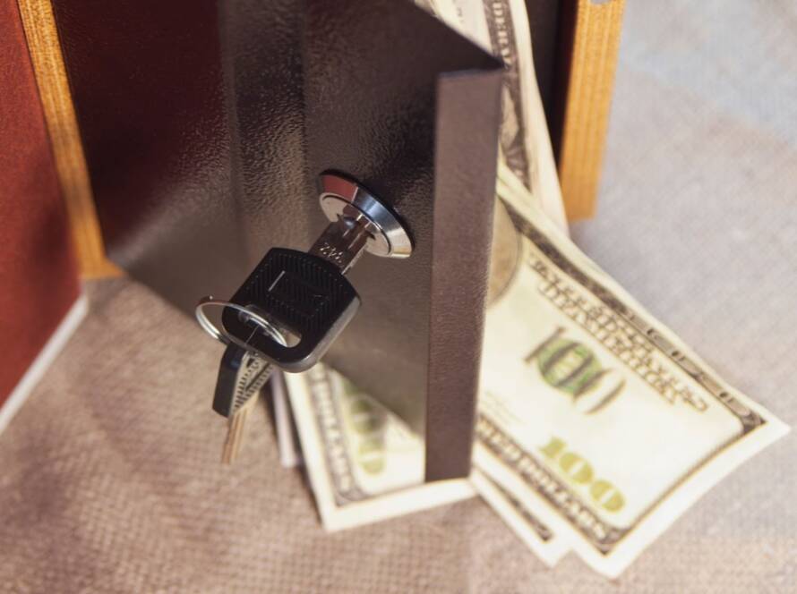 A key in a safe’s lock with dollar bills spilling out as the safe door opens