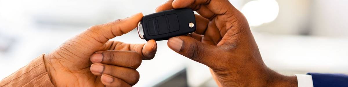 Close-up of a car dealer’s hand handing a reprogrammed key fob to a female customer in a showroom